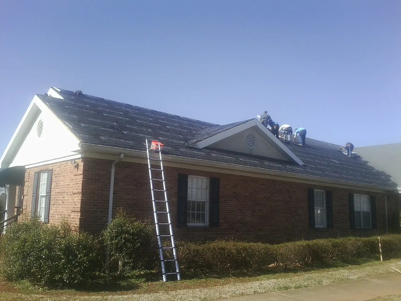 Crew tearing shingles off a brick ranch roof with a ladder set — Metal Roof Repair work by our crew in Royal