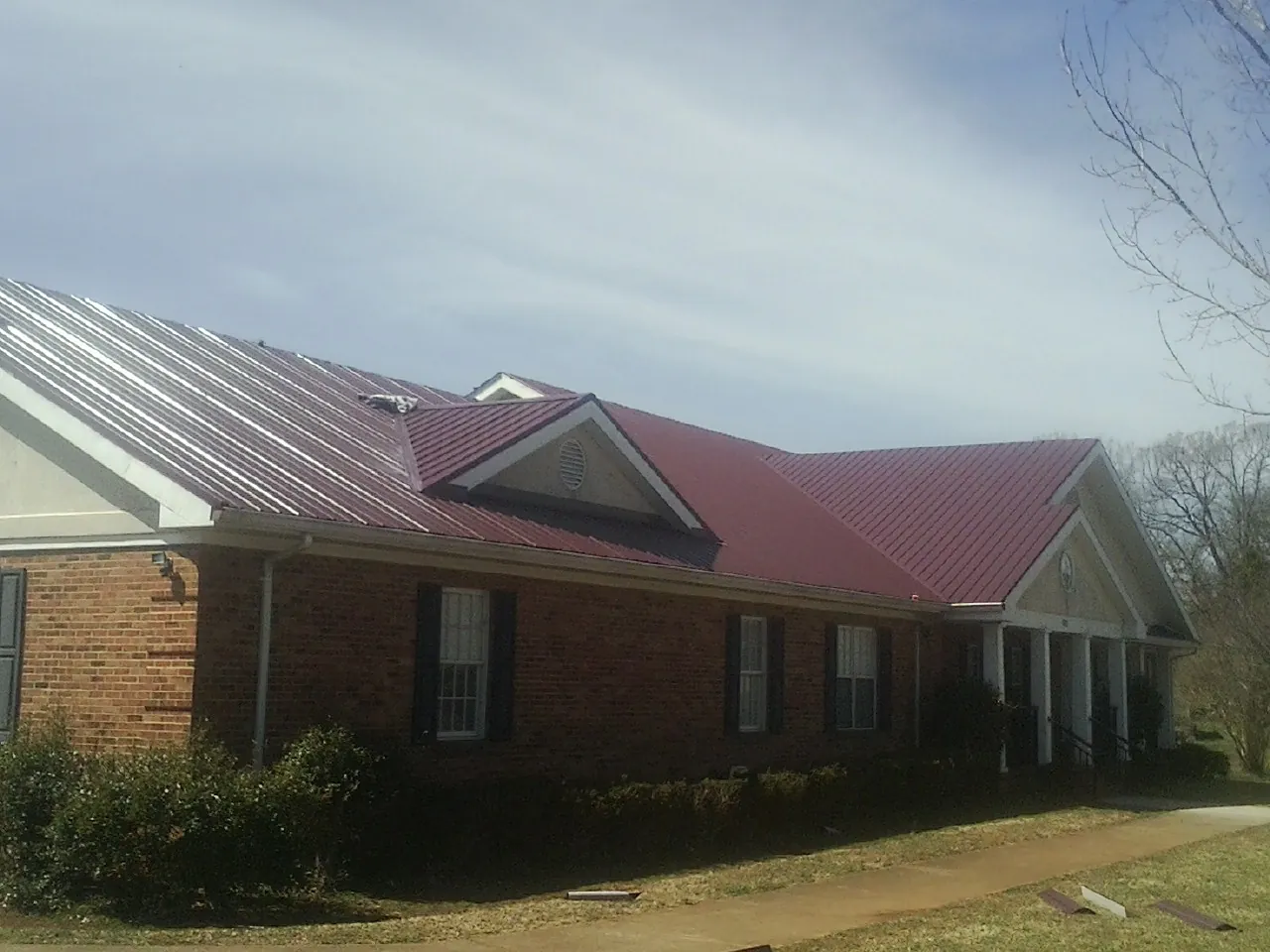 Red metal roof with gabled entries on a long brick building, from a Hail Damage Roof Repair job in Royal