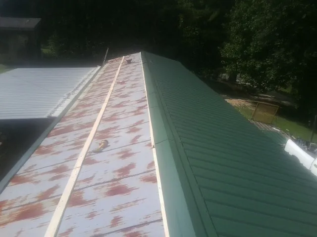 Old rusted panels beside newly installed green metal roofing — Wind Damage Roof Repair by Roofing Brothers in Royal